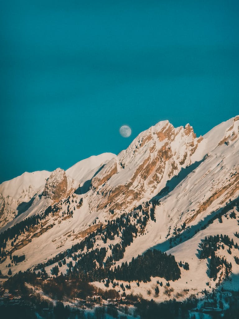 Capture of snow-capped mountains under a clear sky with visible moon.